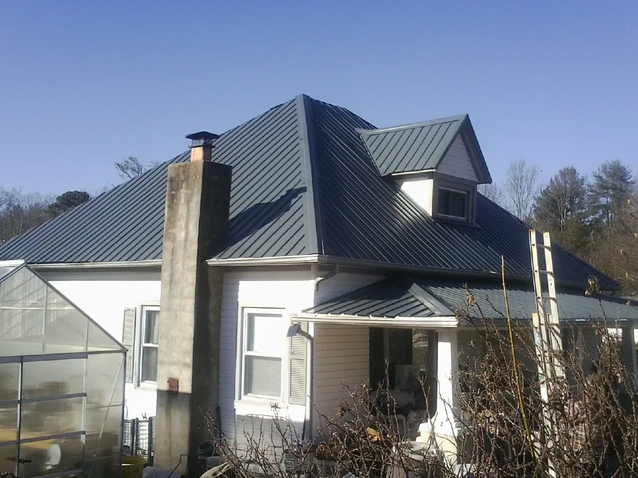 Dark blue standing seam metal roof on a white farmhouse with dormer — Slate & Tile Roof Repair by Roofing Brothers in Blue Mound