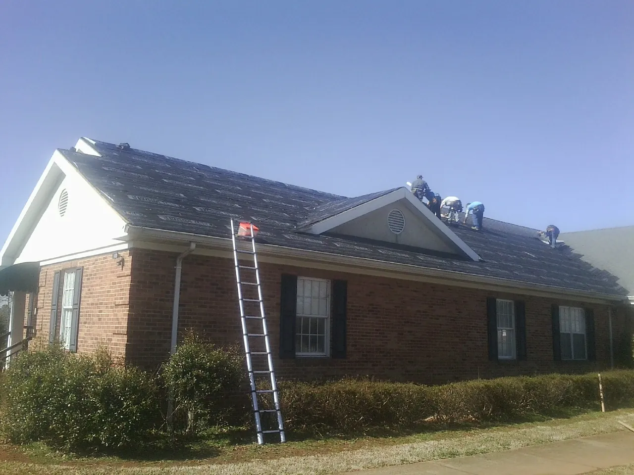 Crew tearing shingles off a brick ranch roof with a ladder set — Emergency Roof Repair work by our crew in Blue Mound