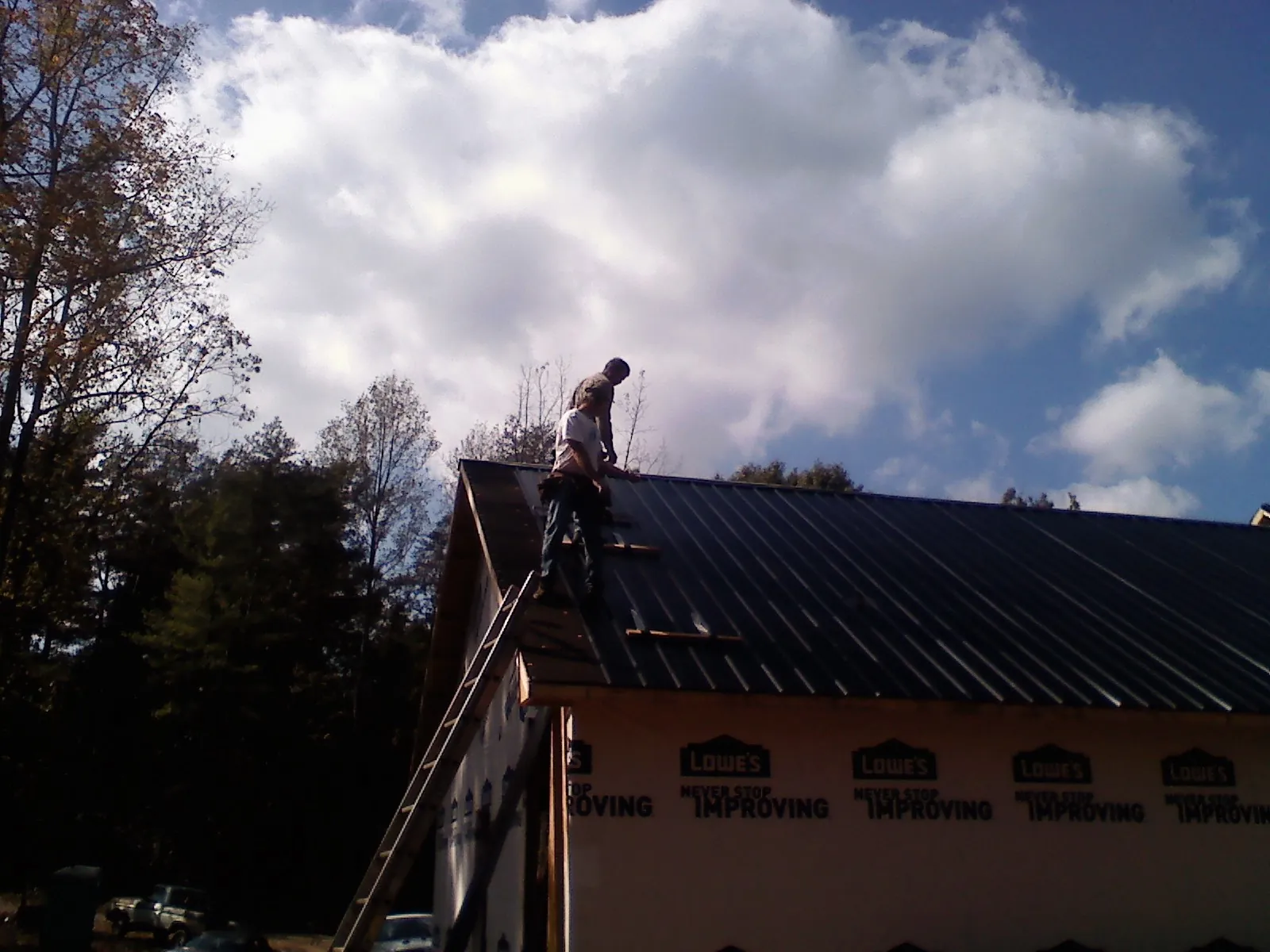 Roofer fastening dark metal panels high against a cloudy sky, from a Roof Inspection job in Blue Mound
