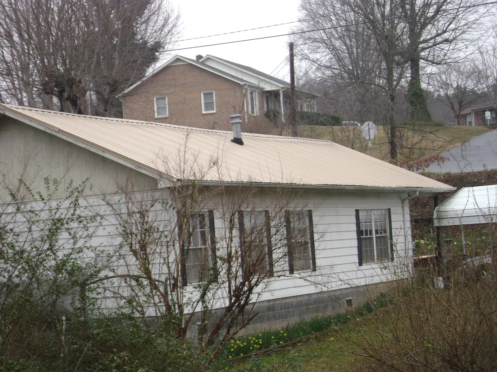 Tan metal roof on a white sided house set into a hillside — Commercial Roofing by Roofing Brothers in Blue Mound