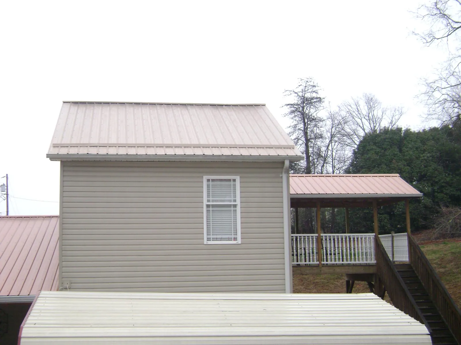 Tan metal roofs on a two story addition and attached porch, from a Roof Replacement job in Blue Mound